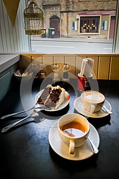 Cup of tea, cappuccino and a red velvet cake on a plate on the window sill of a small cafe.