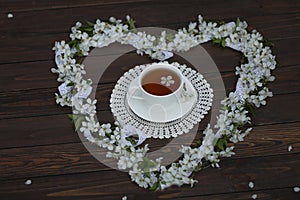 cup of tea with cherry blossom heart shaped decoration on dark brown wooden background