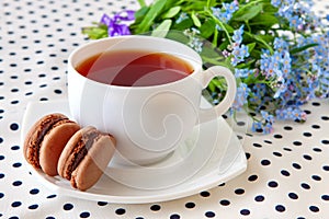 Cup of tea and chocolate macarons with a bouquet of wild forget-me-nots close-up