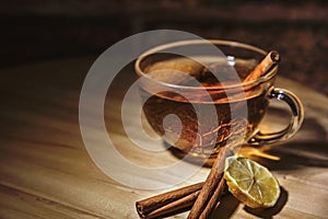 A cup of tea with a cinnamon sticks and a lemon slice on a wooden table, close up, isolated