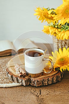 A cup of tea with cinnamon on a wooden tray and an open vintage book with sunflowers, aesthetics