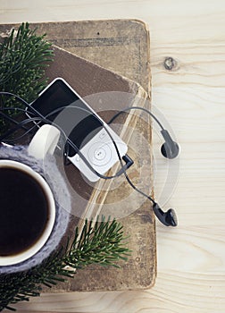 Cup of tea or coffee in a coffee cup cozy, MP3 player, in-ear wired headphones, branch of fir tree, old books.