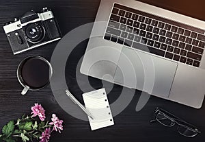 Cup of tea or coffee, photo camera, laptop computer, eyeglasses and pink flowers on black wooden table