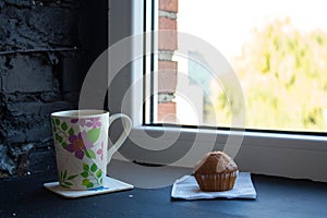 A cup with tea and cupcake near the window