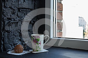 A cup with tea and cupcake near the window