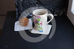 A cup with tea and cupcake near the window