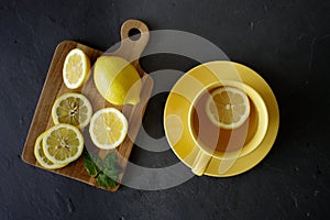 Cup of tea with fresh yellow lemons on black background