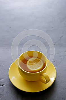 Cup of tea with fresh yellow lemons on black background