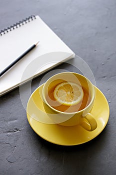 Cup of tea with fresh yellow lemons on black background