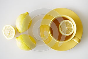 Cup of tea with fresh yellow lemons on white background