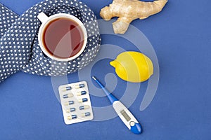 Cup of tea, ginger, lemon and alternative remedies and traditional pills on blue, copy space for text. The concept of seasonal