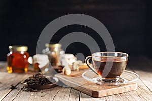 Cup or tea glass Hot brew and dried tea leaves on a wooden plate, placed on a wooden table, on a dark black background