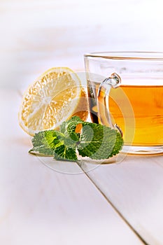 Cup of tea, glass teapot, mint and lemon on a wooden table