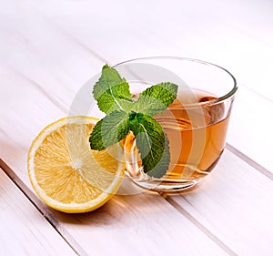 Cup of tea, glass teapot, mint and lemon on wooden table