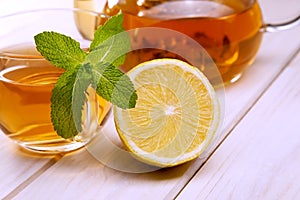 Cup of tea, glass teapot, mint and lemon on wooden table