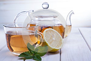 Cup of tea, glass teapot, mint and lemon on wooden table