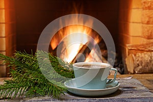 A cup of tea and green fir branches near a cozy fireplace, in a country house, winter or autumn holidays