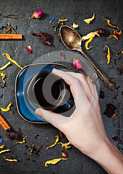 Cup of tea in hand with herbs and flowers on stone background