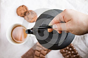 Cup of tea, a hand holding an iron teapot and cookies on the white cloth background