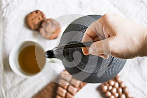 Cup of tea, a hand holding an iron teapot and cookies on the white cloth background