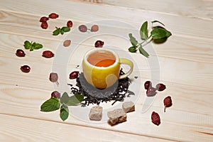 Cup of tea with hip roses, on wooden table. A cup made of real lemon
