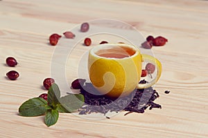Cup of tea with hip roses, on wooden table. A cup made of real lemon