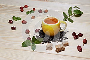 Cup of tea with hip roses, on wooden table. A cup made of real lemon
