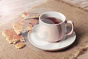 A cup of tea and homemade biscuits on sackcloth napkin on wooden table, closeup