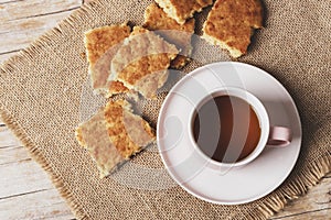 A cup of tea and homemade biscuits on sackcloth napkin on wooden table, top view