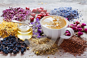 Cup of tea, honey jar, healing herbs and herbal tea assortment