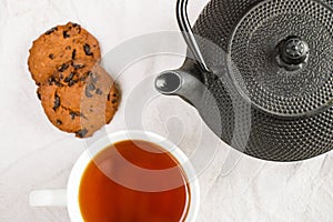 Cup of tea, iron teapot, and cookies on the white cloth background