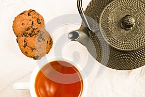 Cup of tea, an iron teapot and cookies on a white cloth background