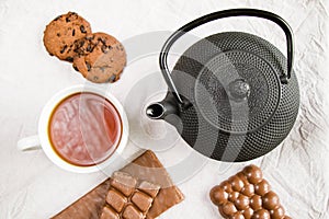 Cup of tea, iron teapot and cookies on the white cloth background, morning food and drink