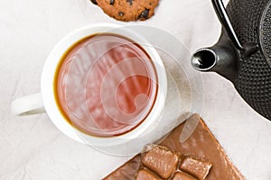 Cup of tea, iron teapot and cookies on the white cloth background, morning food and drink