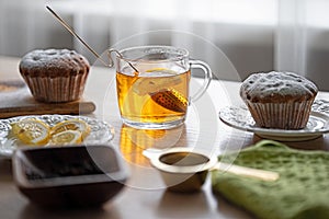 A cup of tea with lemon and cupcakes on a table near the window