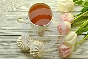 A cup of tea with lemon, fresh tulips and appetizing marshmallows