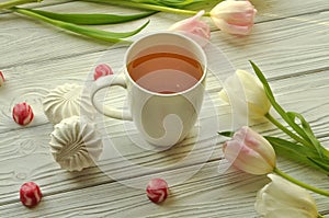 A cup of tea with lemon, fresh tulips and appetizing sweets