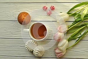 A cup of tea with lemon, fresh tulips and appetizing sweets