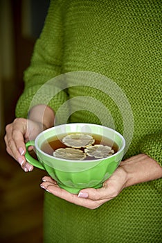 Cup of tea with lemon in hand, yellow autumn leaf.Warm drink concept.