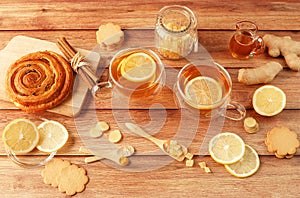 Cup of tea with lemon, honey, ginger root ingredients and sweet cinnamon bun on wooden table. Natural medicine concept