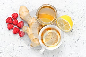Cup of tea with lemon, jar of honey, ginger root with raspberries, healthy ingredients