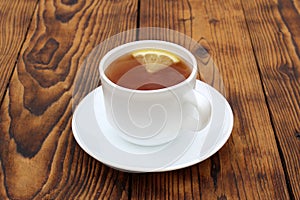 A cup with tea and lemon stands on a wooden table.