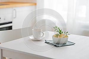 A cup of tea with lemon and a teapot on a white table against the background of a white kitchen with wooden countertop