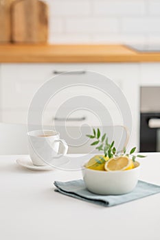 A cup of tea with lemon and a teapot on a white table