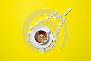 A cup of tea with lemon on a yellow background. Creative photography of tea with sugar.