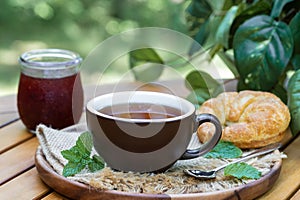 Cup of tea with mint, croissant and jar of jam