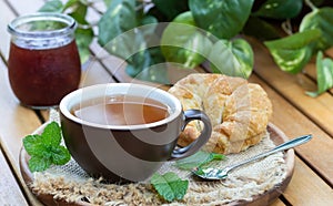 Cup of tea with mint, croissant and jar of jam