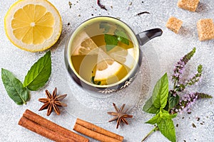 Cup of tea, mint and lemon, brown sugar cinnamon and anise on a grey table