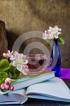 Cup of tea near books and blossom branches of apple tree