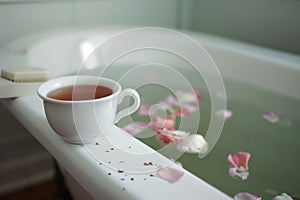 cup of tea near a clawfoot tub with petals floating in bath water